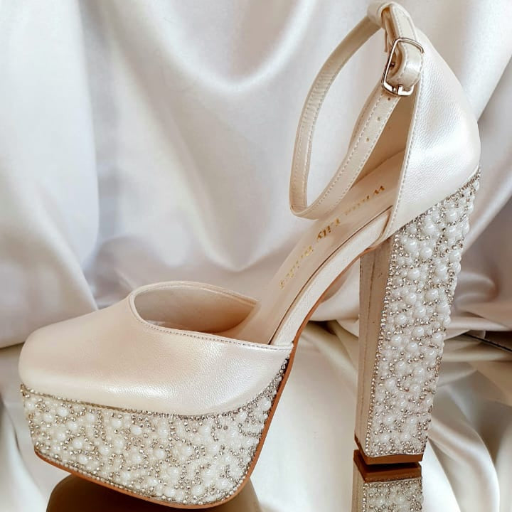 Beige high-heeled shoe with pearl embellishments on a white satin background