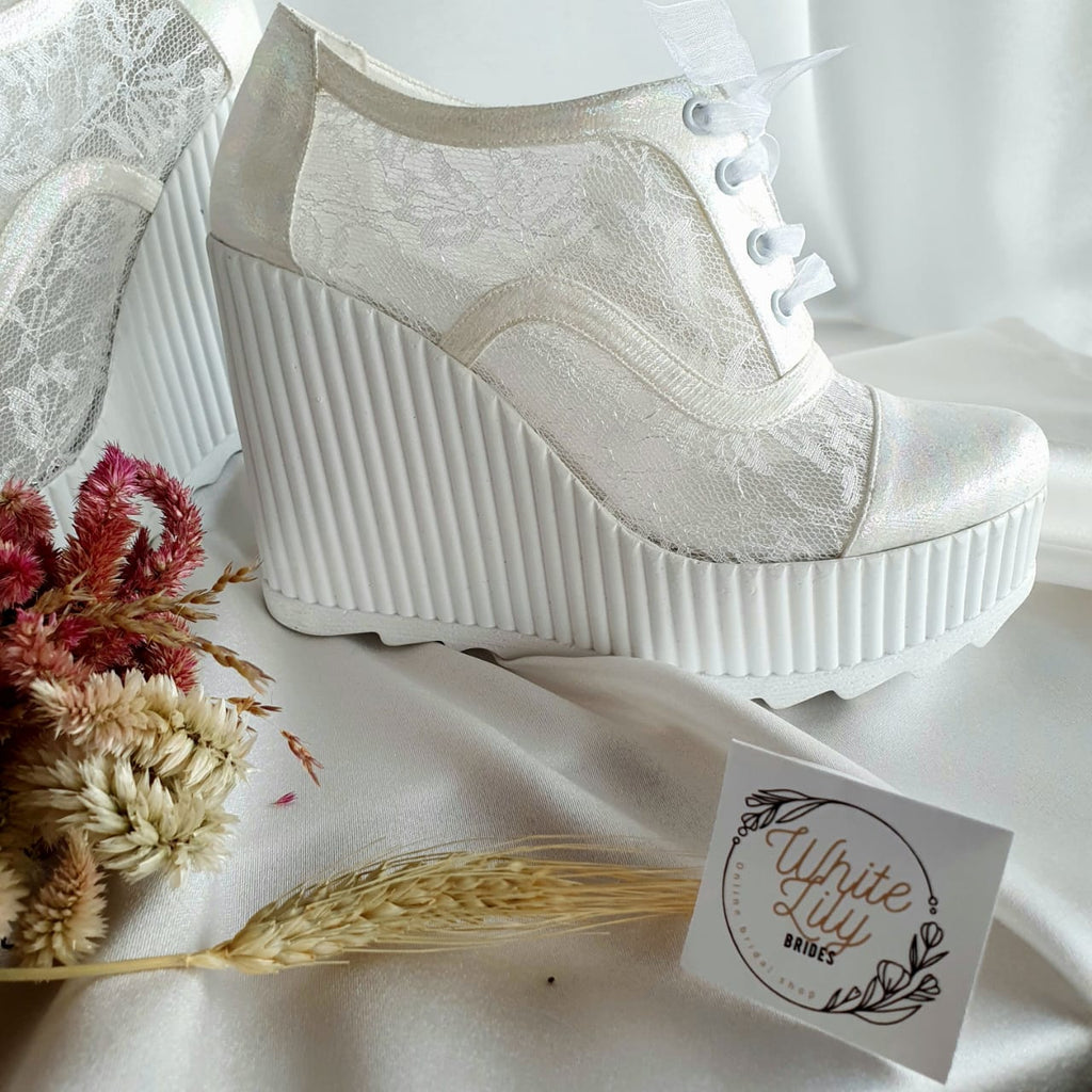 White lace-up shoe with platform sole on a white surface with decorative elements.