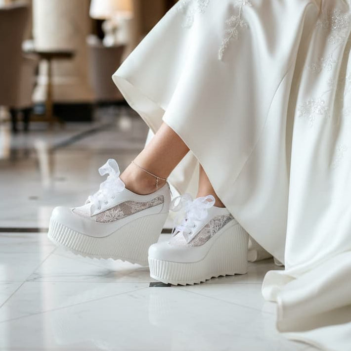 Person wearing a white wedding dress and platform shoes in an elegant indoor setting.