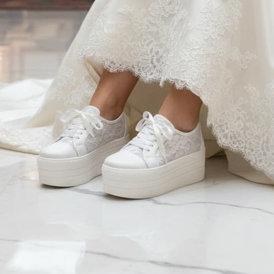 Person wearing a lace wedding dress with white platform sneakers in an elegant indoor setting.
