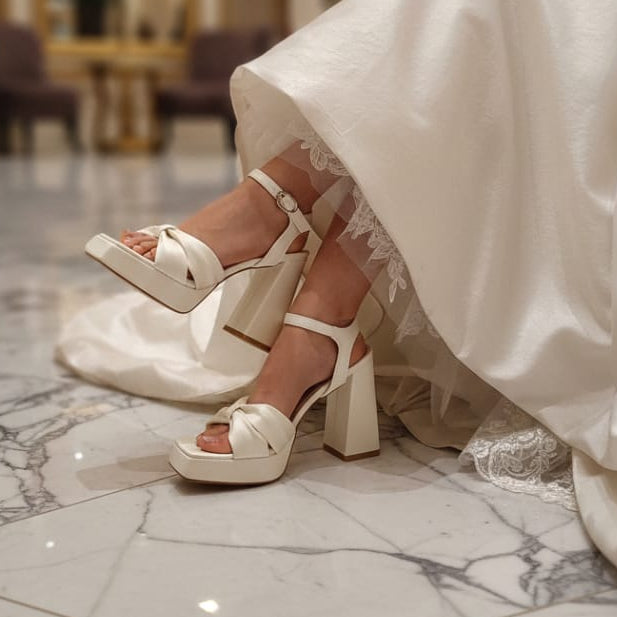 White wedding dress with Bridal high-heeled sandals on a marble floor.